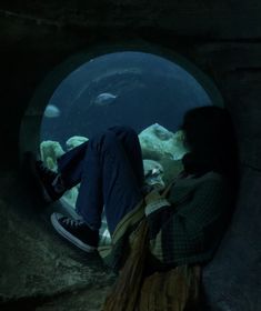 a person sitting in front of an aquarium looking at fish