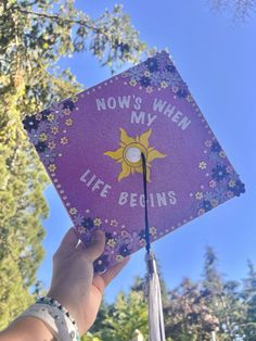 someone holding up a purple graduation cap that says now's when my life begins