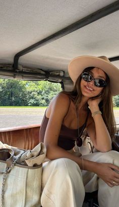 a woman sitting in the back of a car wearing sunglasses and a hat