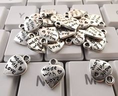 lots of silver charms sitting on top of a computer keyboard with the words made with love written all over them