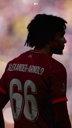 a man with dreadlocks standing in front of a soccer field wearing a red jersey