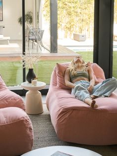 a woman laying on top of a pink couch in a living room next to a window