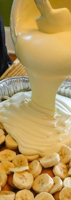 a bowl filled with bananas and cream on top of a wooden table in front of a metal pan