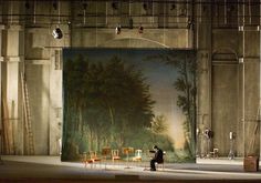 a man standing in front of a painting on a wall next to chairs and ladders