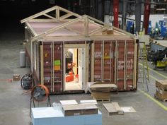 a small house made out of shipping containers in a warehouse with lots of boxes around it