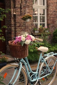 a blue bicycle with flowers in the basket parked on the side of the road next to a brick building