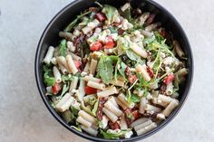 a black bowl filled with pasta salad on top of a white countertop next to a fork