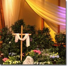 a cross in the middle of a garden with flowers and greenery on either side