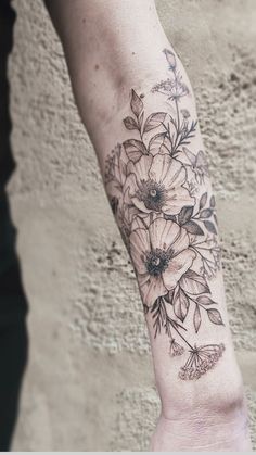 a woman's arm with flowers and butterflies tattooed on her left leg, in front of a concrete wall