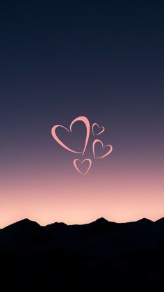 two hearts are drawn in the sky above mountains at night with pink and purple hues