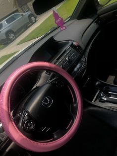 a pink steering wheel cover sitting on top of a car dashboard next to a window