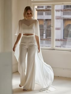 a woman standing in front of a window wearing white pants and a cropped top