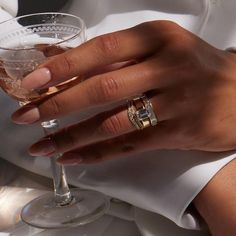 a person holding a wine glass with two wedding rings on it's fingers and wearing a white dress shirt