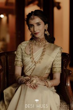 a woman sitting in a chair wearing a white sari and gold jewelry with the caption desi hues