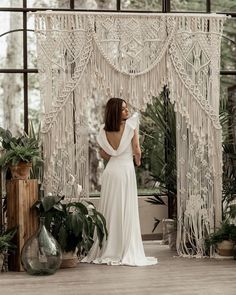 a woman standing in front of a macrame wall hanging from it's ceiling