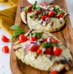 two pizzas with tomatoes, onions and herbs on a cutting board next to a bowl of salsa