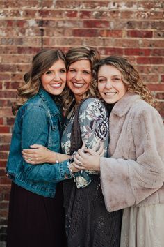 three women standing next to each other in front of a brick wall