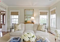 a living room filled with furniture and flowers on top of a table in front of windows