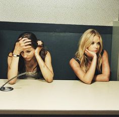 two young women sitting at a table with their hands on their head and one holding her hair