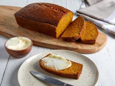 a loaf of pumpkin bread with butter on a plate next to a knife and bowl