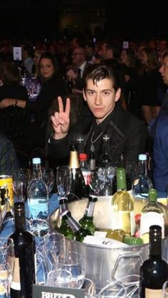 two men sitting at a table with wine glasses and bottles in front of them, making the peace sign