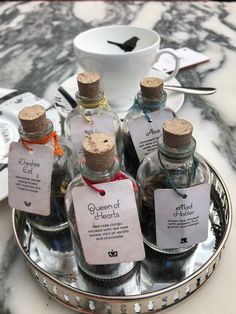 six miniature bottles with labels on them sitting on a tray next to a bowl and spoon