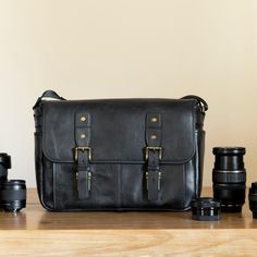 a black leather camera bag sitting on top of a wooden table next to several lenses