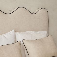 a bed with white linens and black piping on the headboard is shown