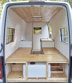 the interior of a small van with wooden tables and drawers in the rear door area