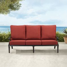 a red couch sitting on top of a cement floor next to a potted plant