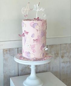 a pink cake with butterflies on it sitting on top of a white pedestal in front of a wall