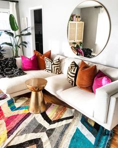 a living room with white couches and colorful pillows on the floor next to a round mirror