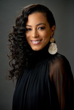 a woman with long curly hair smiling at the camera and wearing large earrings on her ear