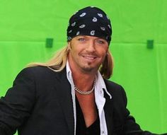 a man with long hair wearing a bandana and looking at the camera while standing in front of a green background