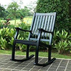 a black rocking chair sitting on top of a brick floor next to bushes and trees