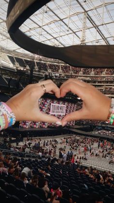 two hands making a heart shape in front of an audience at a sporting event with people sitting on the bleachers