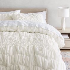 a bed with white comforter and pillows on top of it next to a night stand