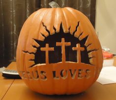 a carved pumpkin with the words jesus loves and crosses on it sitting on a table