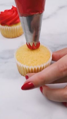 a woman's hand reaching for a cupcake with red icing on it