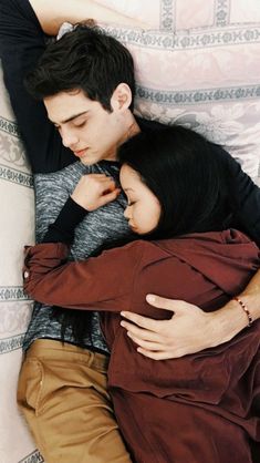 a man and woman laying on top of a bed next to each other with their arms around each other