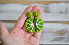 a person holding two green brooches in their hand