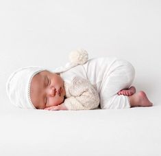 a newborn baby is sleeping with a stuffed animal in it's arms and wearing a white outfit