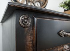 a black dresser with an ornate handle and knobs on the drawer, next to a clock