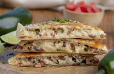 two quesadillas stacked on top of each other with limes and tomatoes in the background