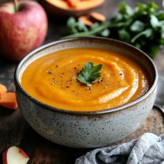 a bowl filled with carrot soup and garnished with parsley next to sliced apples