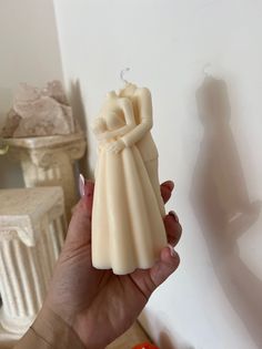 a hand holding a small candle in the shape of a bride and groom on it