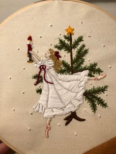 a hand embroidered christmas ornament with a girl in white dress holding a tree