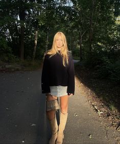 a woman in short shorts and boots is standing on the road with her legs crossed