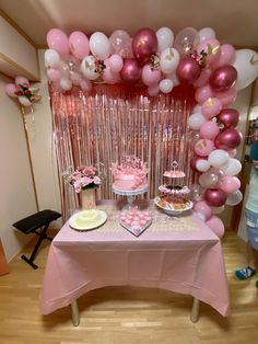 a table topped with lots of pink and white balloons next to a cake on top of a plate