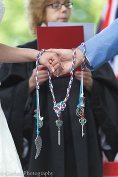 two people holding hands while wearing graduation gowns and bracelets with beads on them